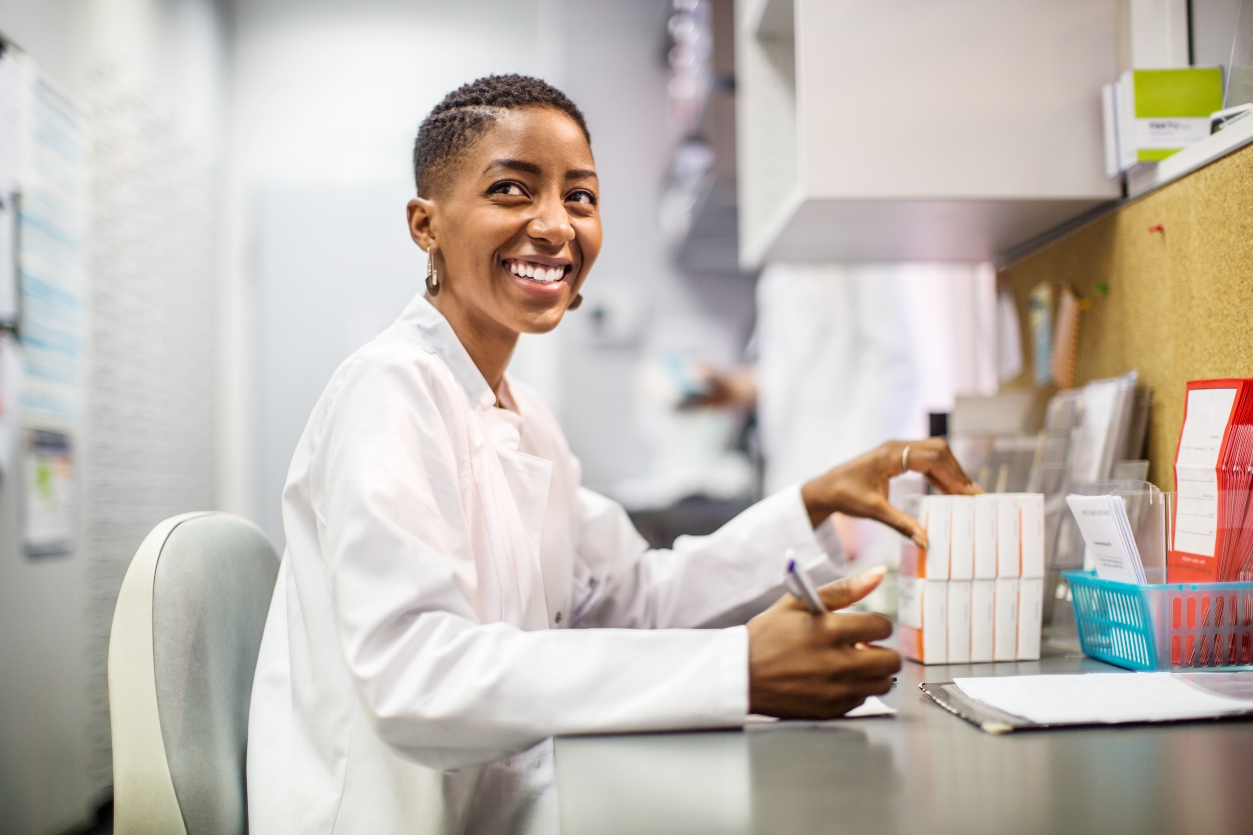 Woman pharmacist sitting at her desk smiling. Woman pharmacist sitting at her desk smiling.